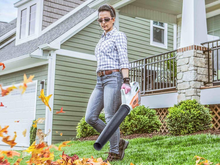 Woman using a leaf blower on her lawn in a TV broadcast spot.